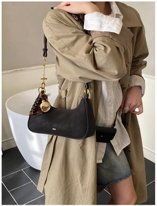 Détail d'un sac hobo noir avec des breloques vintage sur la bandoulière porté par un mannequin