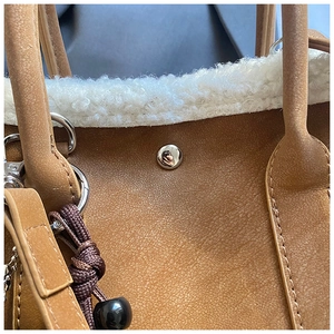 Detail of brown leather tote bag with white faux fur trim and silver magnetic buckle