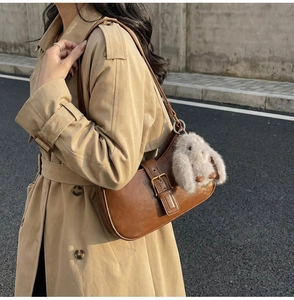 Detailed view of dark brown leather underarm bag with decorative metal buckle and plush bunny charm