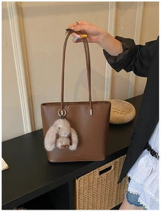 Close-up of brown pebbled leather bucket bag with cute plush rabbit charm accessory