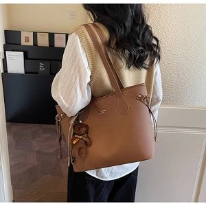 Detail of brown litchi pattern leather tote bag with cute plush bear charm on a model