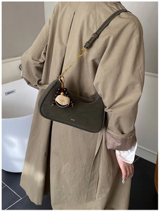 Sac hobo en cuir mat vert foncé avec pendentif en bois porté sur un trench-coat