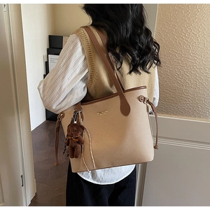 Detail view of stylish tote bag with plush bear charm and contrast brown leather trim
