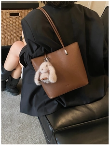 Brown litchi leather bucket bag with plush rabbit charm worn on a black blazer