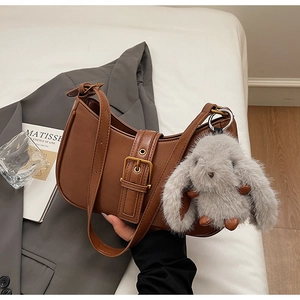 Detailed view of a brown faux leather crescent bag with a plush rabbit charm and strap