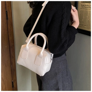Close-up of a cream-white pebbled leather bowling bag held by a model in a minimal outfit