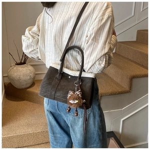 Close-up of brown suede handbag with white faux shearling trim and plush monster charm