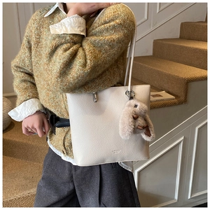 Detail of beige lychee leather tote bag with plush rabbit charm worn on shoulder