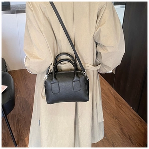 Rear view of a black pebble leather Boston bag styled with a beige trench coat