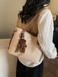 Beige canvas tote bag with brown leather trim and cute teddy bear charm accessory