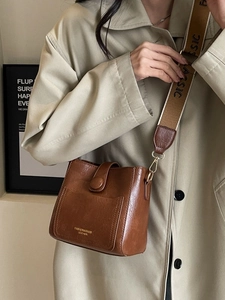 Brown bucket shoulder bag with wide woven strap and minimalist front pocket detail