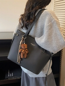 Black leather tote bag with teddy bear charm and brand logo carried by model