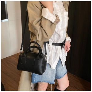 Detail of black lychee grain leather handbag featuring circular handles and metal strap