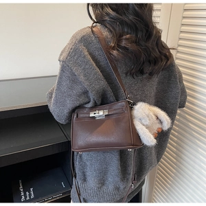 Detail of dark brown leather handbag featuring silver twist lock and cream furry charm