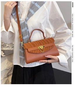 Detail of brown fashion flap handbag with gold clasp and chain on model's hand