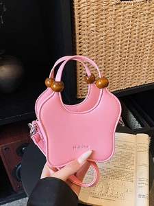 Pink PU leather handbag with wooden bead handles and crossbody strap in lifestyle setting