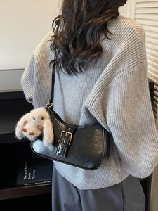 Minimalist black leather underarm bag with gold buckle and plush rabbit charm on a model