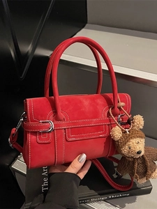 Red matte leather tote bag with white stitching and bear charm on black books