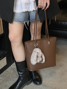 Brown lychee leather bucket tote bag with gray rabbit plush charm and long shoulder strap
