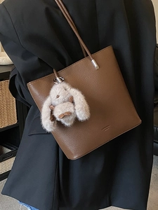 Brown litchi leather bucket bag with plush rabbit pendant worn on black blazer