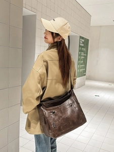 Large dark brown vintage leather tote bag with front pockets shown in outdoor street style