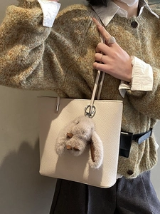 Chic beige lychee leather bucket bag with a plush grey bunny charm for autumn style