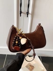 Sac hobo rétro en daim marron foncé avec pendentif bohème sur fond de porte blanche