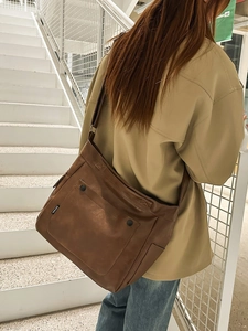 Brown leather crossbody tote bag with flap and decorative buckles on a female model