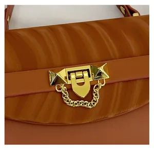 Close-up of golden hardware lock with rivets and chain on caramel textured shoulder bag