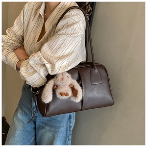 Detail of dark brown leather Boston bag featuring a plush rabbit pendant and vertical stitching