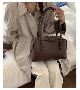 Model wearing dark brown leather shoulder bag with spacious rectangular design and top handles