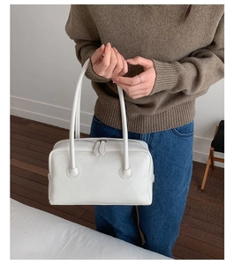 Detail of white leather shoulder bag featuring dual zipper closure and slim long handles