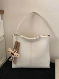 Minimalist off-white leather tote bag with wide strap and cute brown rabbit charm accessory