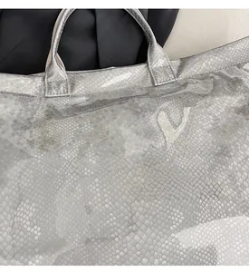 Close-up of glossy grey snake skin texture with white TOTE BAG lettering on a handbag