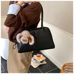 Close-up of black leather Boston bag with cute plush bunny charm and shoulder strap