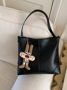 Large black leather tote bag with vertical stitching and cute rabbit charm on a sofa