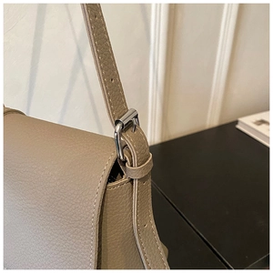 Close-up of brown pebbled leather texture with white stitching and silver buckle on bag