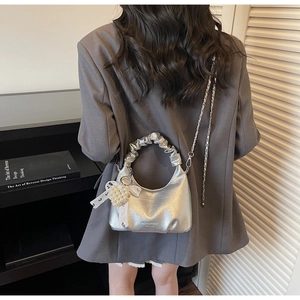 Close-up of silver pleated handbag with pearl heart charm and lace bow on a gray blazer