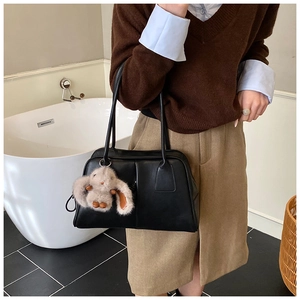 Detail of a chic black Boston bag with a cute plush bunny charm and dual long shoulder straps