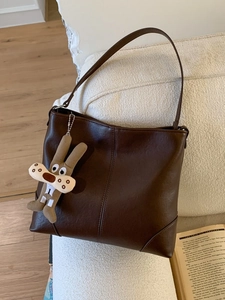 Deep brown soft leather tote bag for women with cute rabbit charm on white sofa