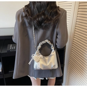 Detail of silver metallic handbag with ruched handle and elegant pearl heart pendant
