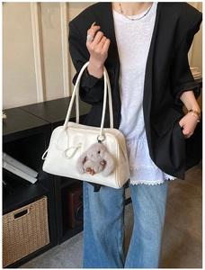 Close-up of white Boston bag with plush rabbit charm held by model in casual suit
