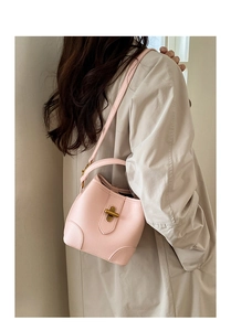 Pale pink lychee grain leather bucket bag with gold twist lock worn with a beige trench coat