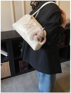 Close-up of white Boston bag with plush rabbit charm worn on a female model shoulder