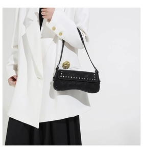 Close-up of black leather underarm bag with silver rivets styled on a white blazer