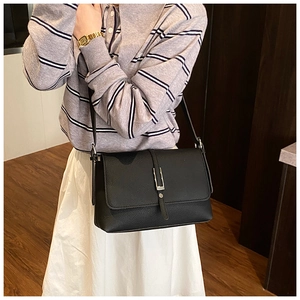 Detail of black pebbled leather shoulder bag with sleek silver buckle on model