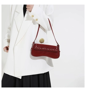 Close-up of deep red leather baguette bag with silver studs on white blazer
