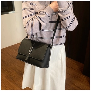Sac à bandoulière en cuir noir grainé avec boucle en métal argenté porté par un mannequin