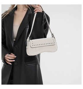 Detail of a cream-colored vintage handbag with silver rivets and smooth adjustable strap