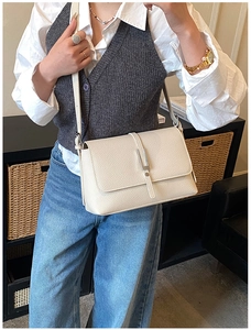 Detail of a beige litchi grain leather crossbody bag with silver buckle on a female model